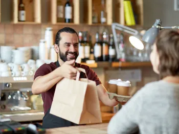 Café owner handing a customer coffee and a takeout order